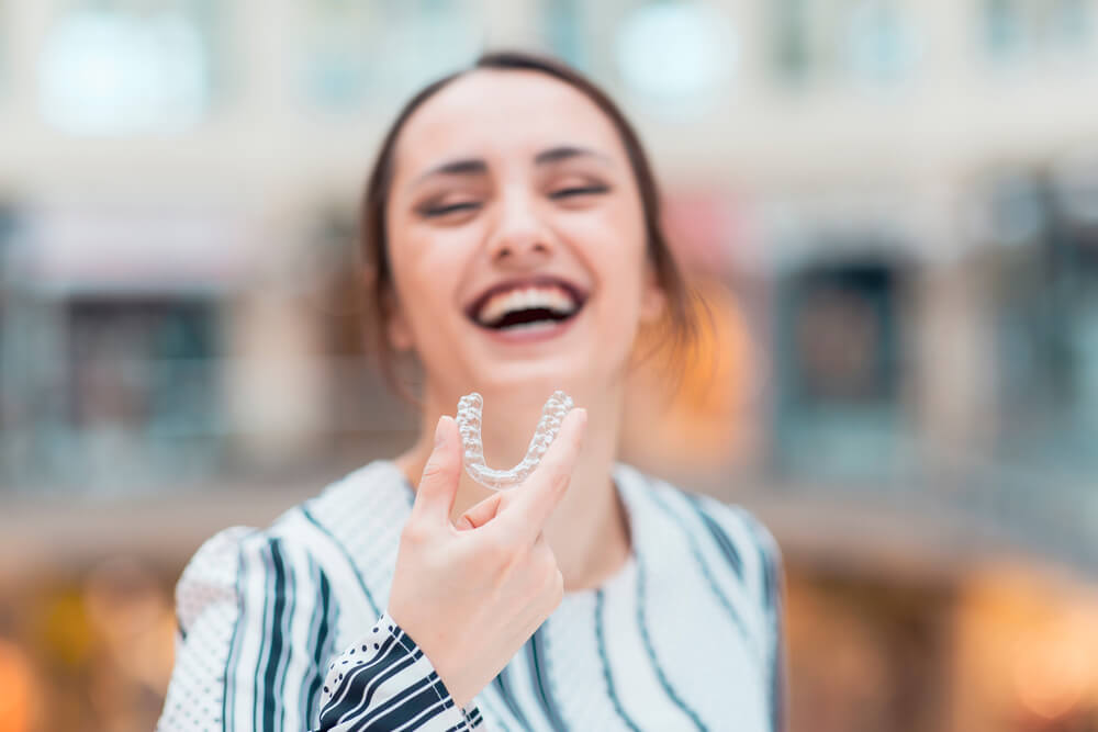 Beautiful smiling woman is holding an invisalign bracer